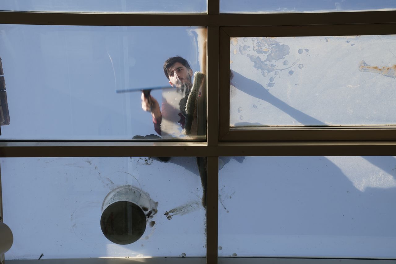 services-02 A male window cleaner washing the exterior glass roof from above with a tool during daylight.
