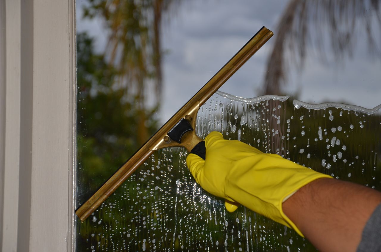 hero-img-01 Close-up of hand cleaning window with squeegee outdoors using yellow gloves.